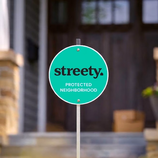 A Streety yard sign reading Protected Neighborhood, staked in front of a house